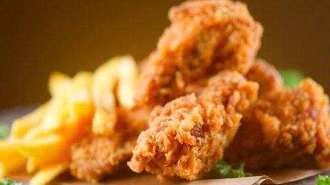 Crispy fried chicken wings and legs with french fries on a wooden table rotation 360 degrees. Breaded Crispy chicken,  fried potato tasty dinner. 4K UHD video footage. Ultra high definition 3840X2160