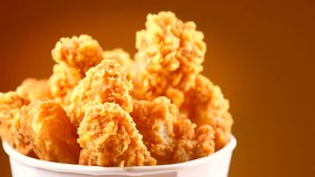 Bucket of Crispy fried chicken wings and legs over brown background rotation 360 degrees. Breaded chicken tasty dinner UHD video footage. Ultra high definition 3840X2160 4K