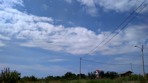 Time lapse of white fluffy clouds over blue sky with village background