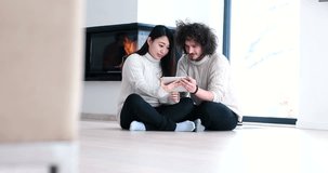 Beautiful multietnic couple using digital tablet talking and smiling while sitting on the floor near fireplace