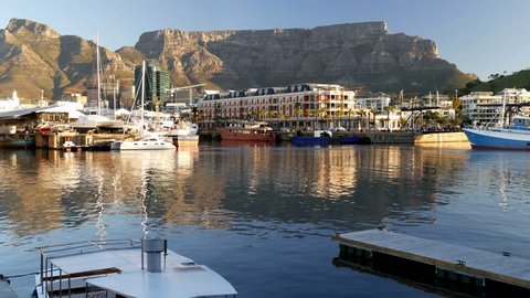 CAPE TOWN, SOUTH AFRICA CIRCA AUGUST 2017, Marina with pontoon, small boat, Cape Grace hotel, Catamarans in water & on land, banking, financial towers city centre & mountain to blue skyline, evening