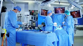 Surgical hospital specialist team in scrubs in the operating theatre performing laparoscopic surgery using video monitor playback and Endoscope and Laparoscope instruments RED DRAGON