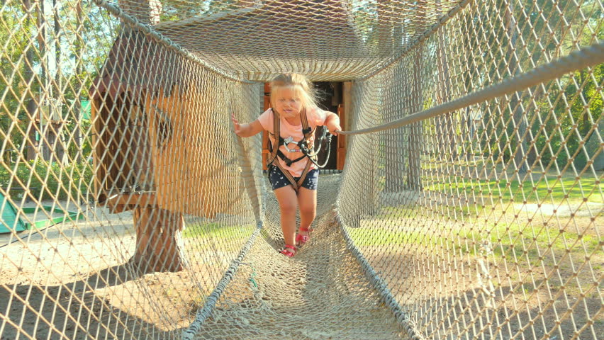 Little girl in equipment moves through ropeway in park