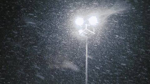 Snow falling with streetlight beams at night. Loop able snow fall background video.
