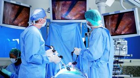 Professional hospital specialist team in scrubs in the operating theatre performing laparoscopic surgery using video monitor playback and Endoscope and Laparoscope instruments RED DRAGON