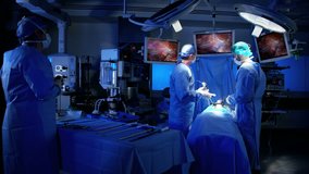 Surgical Multi ethnic male and female in healthcare hospital performing Laparoscopic operation carried out using Endoscopy and Laparoscope instrument with video monitor playback RED DRAGON