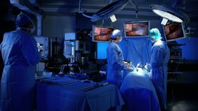 Laparoscopy surgical training operation transmitted on hospital monitor performed by surgeons Caucasian males and African American female wearing surgical mesh and scrubs RED DRAGON