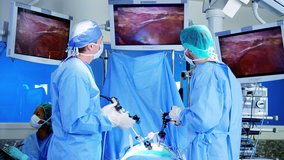 Professional Multi ethnic hospital specialist team in scrubs in the operating theatre performing Laparoscopy surgery using video monitor playback and Endoscope and Laparoscope instruments RED DRAGON