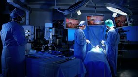 Multi ethnic European Caucasian surgical team in scrubs performing laparoscopic surgery on the patient in operating theatre using video camera playback technology RED DRAGON