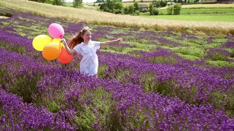 Pretty child girl runs with colorful balloons in lavender field, summer freedom concept