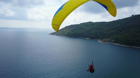 Cinematic tracking shot of paraglider, flying over tropical sea coast. Stunning view from height, recreational aircraft soar in ascending air flow from warm water. Pilot turn and plane along shore