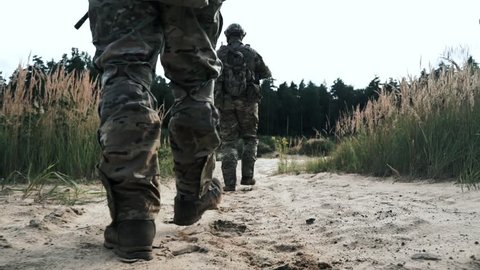 Military soldiers with weapons walking on sand back view. Soldiers with sniper rifle walking on sand. Soldiers with military gear walking on sand