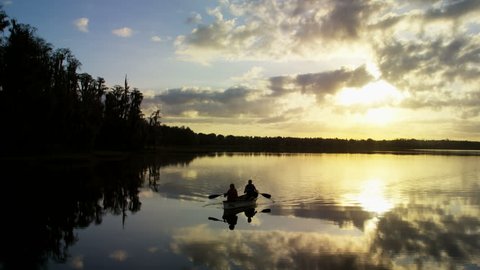 Silhouette of retired Caucasian American couple enjoying the sunrise having canoeing trip on the lake outdoors RED DRAGON