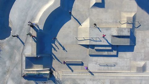 Aerial 4K Drone footage of Sidewalk Surfers. The moving drone captures the action, the shadows and the skills of skateboarders performing stunts over cement geometric shapes.