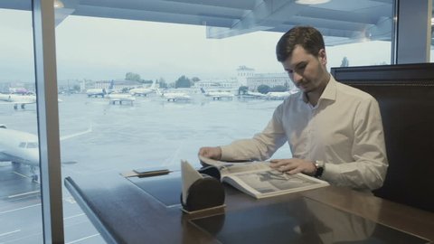 Businessman waits for boarding in the airport and read the magazine