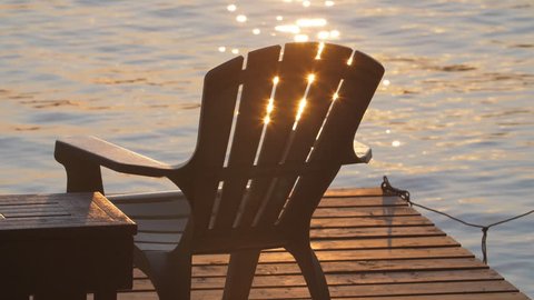 Slow motion golden sparkles from lake with dock and Muskoka chair. Summer in cottage country, Ontario, Canada.
