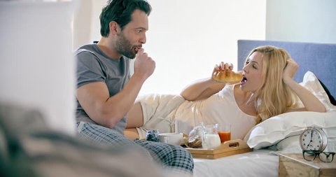 Beautiful man and woman eating breakfast with brioches in bed.Couple in love morning wake up at home in bedroom. Caucasian girlfriend and boyfriend people liying on bed. Lovely strokes. 4k video