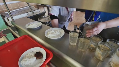 Workers of the school canteen serve schoolchildren by imposing dishes on their plates.