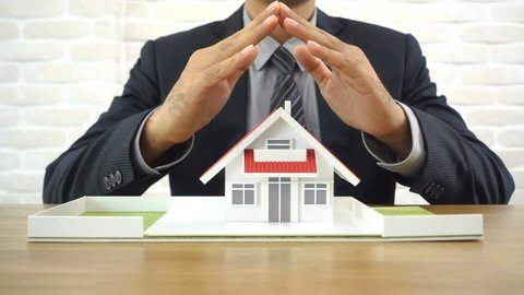 Businessman covering and protecting home with his hands - property and real estate insurance concept