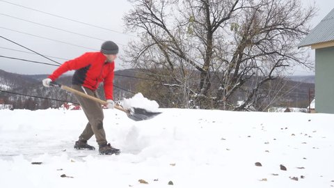 Man with a shovel removing snow from a roof. Caucasian men using to shovel heavy snow off roof.  People with plastic shovel tool push clean snow from roof. 스톡 비디오