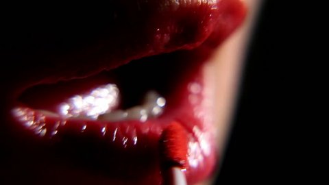 woman paints her lips with lipstick on a black background, close-up 2