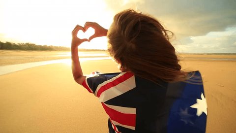 Female on beach makes heart shape finger frame, Australian flag
Young woman on the beach at sunset makes a heart shape finger frame towards the sunset, she is wrapped in an Australian flag.
