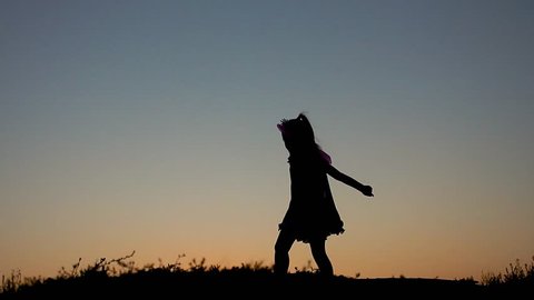 Silhouette of happy little girl dressed in a fairy costume with wings. The child presents himself as a sorceress, the concept of children's play and imagination.