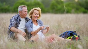 Happy retired Caucasian European couple on hike vacation using smartphone for video chat resting outdoors RED DRAGON