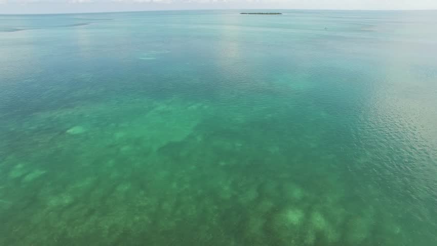 Aerial video over the ocean in the Florida Keys.  Rock formations under the water are visible. 