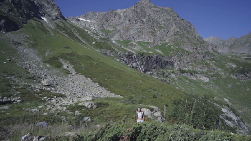 young woman backpacer in the mountains collects water in a mountain river