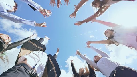 Friendly graduates of the senior school put their hands on each other and open them against the blue sky. Sunny daylight. College Students Teamwork Stacking Hand Concept.