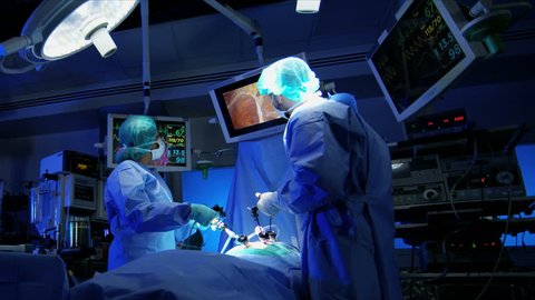 Medical surgical training hospital performing Laparoscopic operation by multi ethnic male and female specialist team in scrubs using video monitors technology RED WEAPON