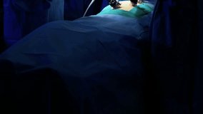 Caucasian hospital Surgical team in scrubs in the operating theatre performing Laparoscopy surgery using both Endoscope and Laparoscope with video monitor playback RED DRAGON