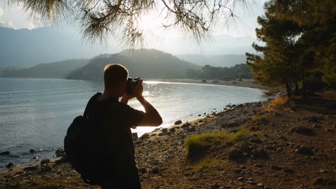 traveler photographer shoots beautiful sunset on the shore of a mountain lake