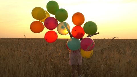 young girl in the dress with colorful ballons is running across the field. Freedom concept