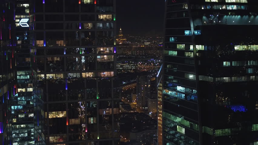 Unique Aerial flight around and approach to windows of Moscow City business center. Evening illumination. Offices from outside. Managers employees work. Quadcopter drone beautiful 4K shot