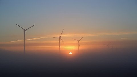 Wind turbines slowly spinning during a foggy sunrise in the Dutch countryside.