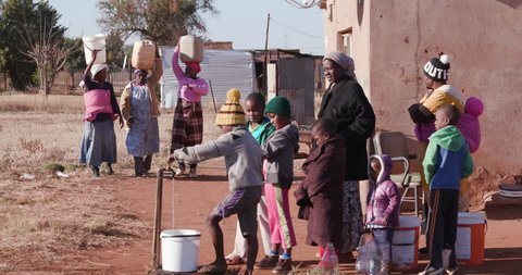 
Poor people in Africa unable to maintain social distance to prevent Covid 19, due to overcrowding and poverty Young african boys drinking water from a tap while woman line up to collect water in cont