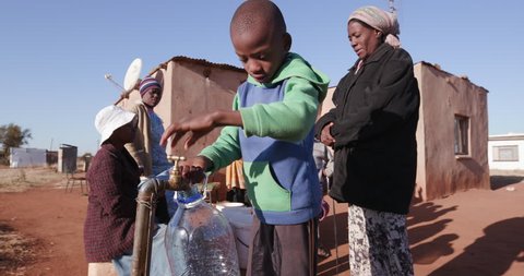 Poor people in Africa unable to maintain social distance due to water crisis The struggle for water.Young african boy collecting water from a tap while woman line up to collect water in containers 