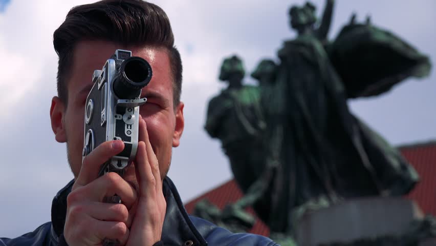 A young handsome man shoots a video with a camera - closeup from below - a statue in the blurry background