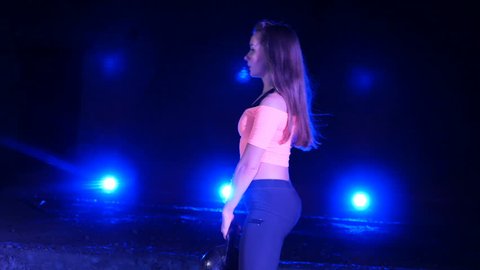 Athletic, beautiful, young woman doing various strength exercises with weights. At night, in the light of searchlights, in light smoke, fog, in an old abandoned hangar, the building