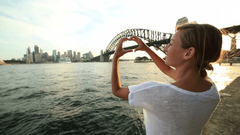 Young woman in Sydney harbour makes a heart shape finger frame on the Sydney skyline.