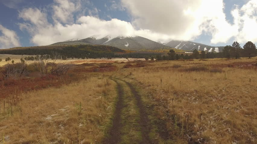 Beauty drone executed lifting shot of San Francisco Peaks mountain area outside of Flagstaff Arizona. Dramatic clouds, autumn or fall leaves on aspen, snow on ski runs in background.