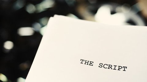 White cover paper with script title text close up over blurred unrolled movie filmstrip background