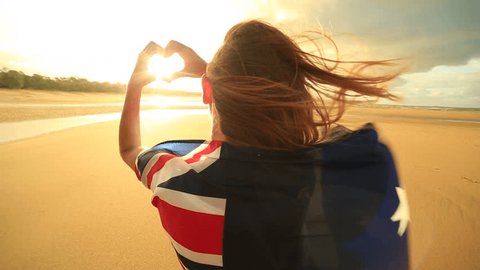 Female on beach makes heart shape finger frame, Australian flag
Young woman on the beach at sunset makes a heart shape finger frame towards the sunset, she is wrapped in an Australian flag.
