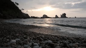 Static background video of beach sunset, romantic cove, sound of the pebbles scrambling on the shore line Landscape of spanish beach taken in the north Asturias. beautiful inlet small bay. 