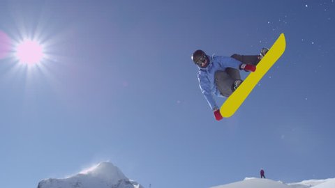 SLOW MOTION: Young pro snowboarder riding the half pipe in big mountain snow park, jumping high out of the halfpipe wall, performing tricks and rotations with grabs in sunny winter