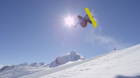 SLOW MOTION: Young pro snowboarder riding the half pipe in big mountain snow park, performing spraying trick on halfpipe wall lip in sunny winter