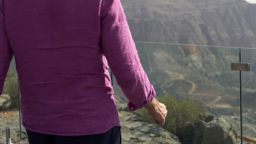 Young man stretching arms on terrace and enjoying canyon view 
