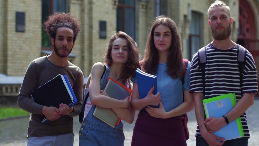View of students posing for camera. university building on background. Group of multiethnic college friend standing in college park.